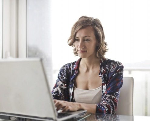 Self employed woman, smiling filling in her pay stub generator templates on a laptop